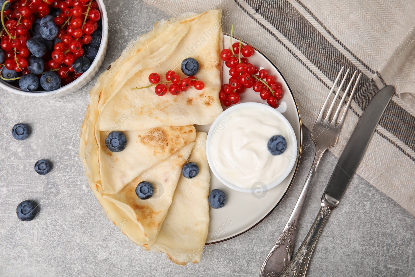 Photo of Delicious crepes with natural yogurt, blueberries and red currants on grey table, flat lay