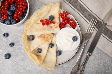 Delicious crepes with natural yogurt, blueberries and red currants on grey table, flat lay