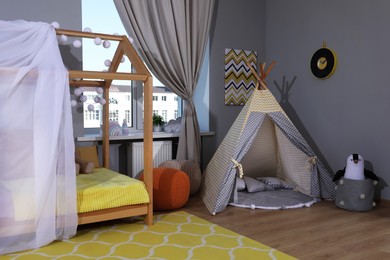 Photo of Stylish child room interior with comfortable house bed and play tent