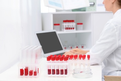 Test tubes with blood samples and scientist working on computer in laboratory