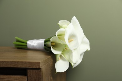 Beautiful calla lily flowers tied with ribbon on wooden table near olive wall