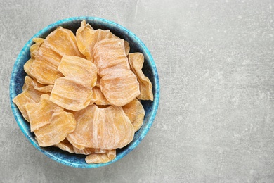 Photo of Delicious dried jackfruit slices in bowl on light grey table, top view. Space for text