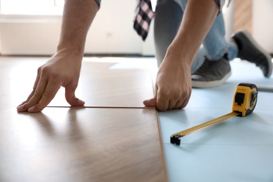 Worker installing laminated wooden floor indoors, closeup