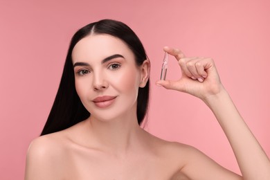 Photo of Beautiful young woman holding skincare ampoule on pink background