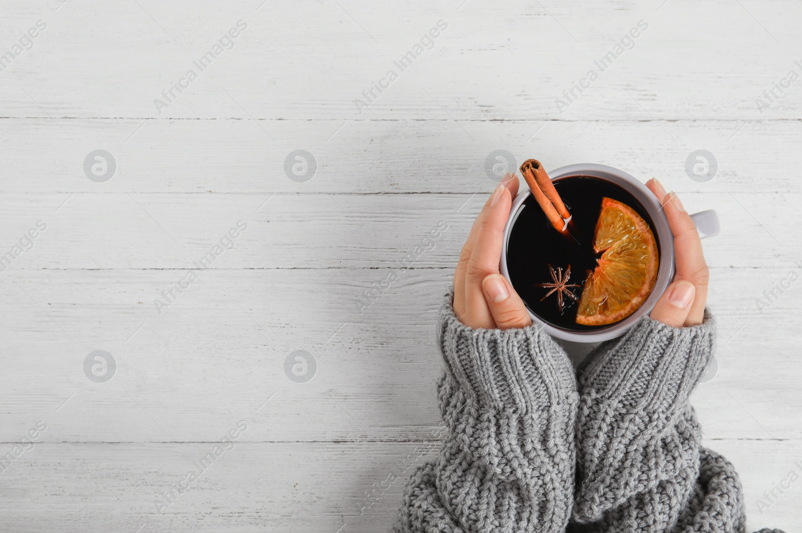 Photo of Woman holding cup of hot mulled wine at white wooden table, top view with space for text. Winter drink