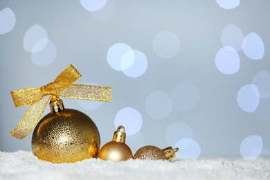 Beautiful golden Christmas balls on snow against blurred festive lights. Space for text