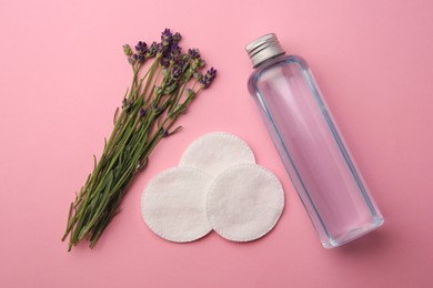 Photo of Bottle of makeup remover, cotton pads and lavender on pink background, flat lay