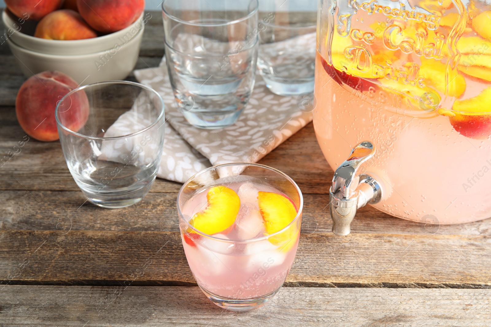 Photo of Peach cocktail in glass and jar with tap on table. Refreshing drink