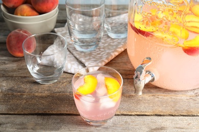 Peach cocktail in glass and jar with tap on table. Refreshing drink