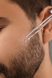 Photo of Man applying cosmetic serum onto face, closeup