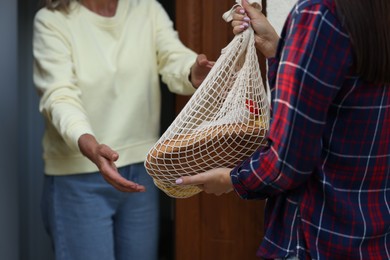 Young woman with net bag of products helping her senior neighbour outdoors, closeup