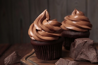 Photo of Delicious cupcakes with cream and chocolate pieces on wooden table, closeup