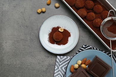 Photo of Delicious chocolate candies powdered with cocoa, sieve and ingredients on grey table, flat lay. Space for text