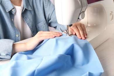 Seamstress working with sewing machine at white wooden table indoors, closeup