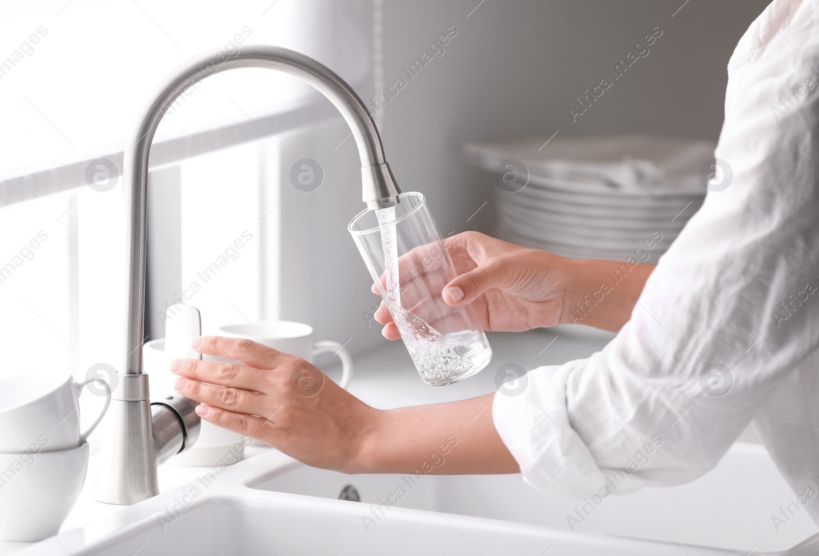 Photo of Woman pouring water into glass in kitchen, closeup