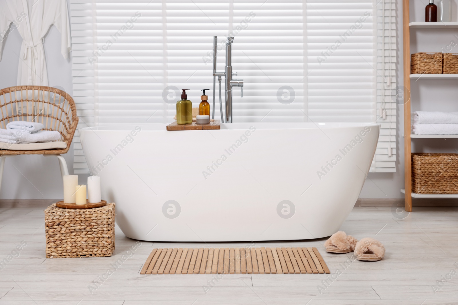 Photo of Stylish bathroom interior with bamboo bath mat and white tub