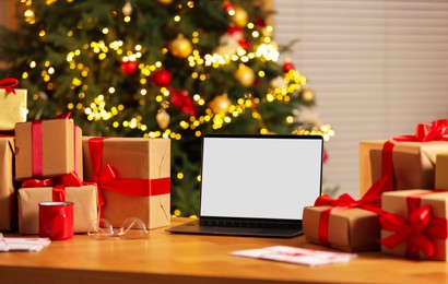 Photo of Christmas time. Laptop with blank screen, gift boxes and letters on table at home