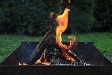 Photo of Metal brazier with burning firewood outdoors, closeup