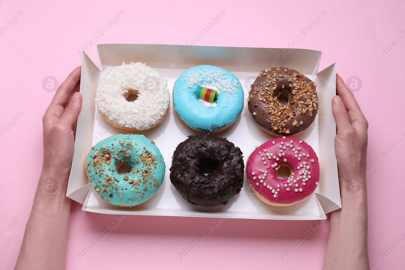 Photo of Woman holding box with tasty glazed donuts on pink background, top view