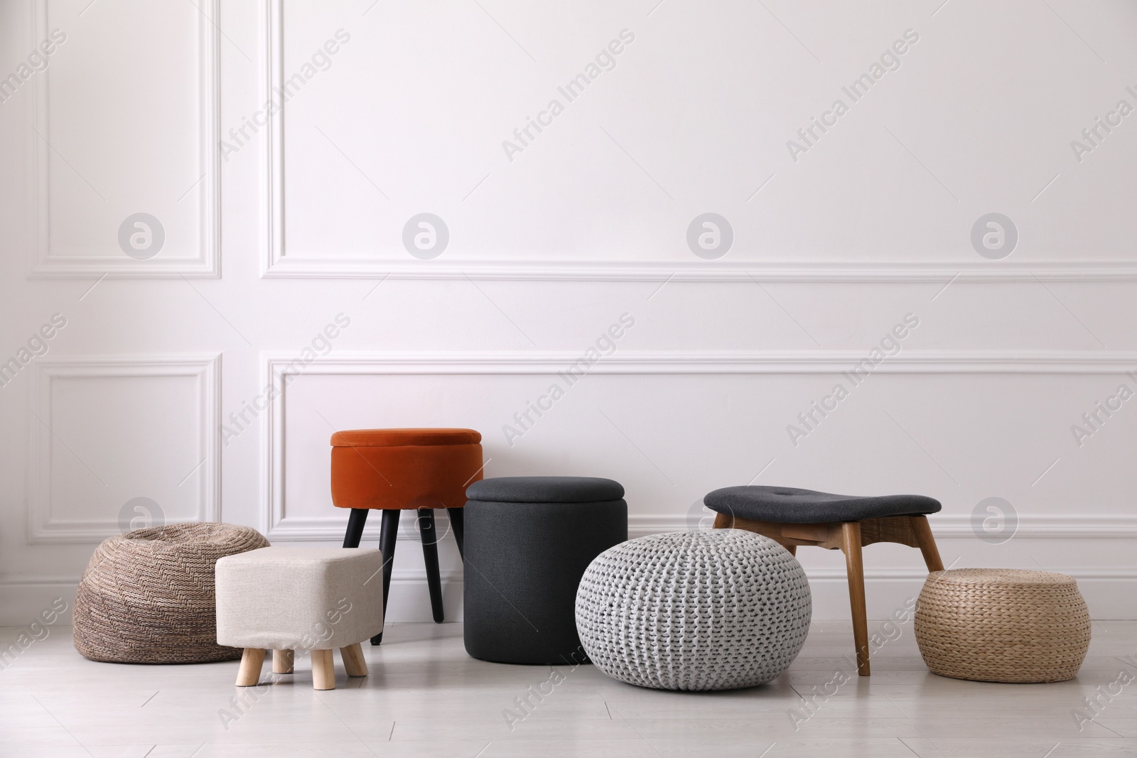 Photo of Different stylish poufs and ottomans near light wall