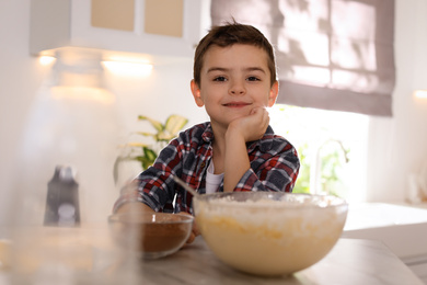 Photo of Cute little boy at table with cooking ingredients in kitchen