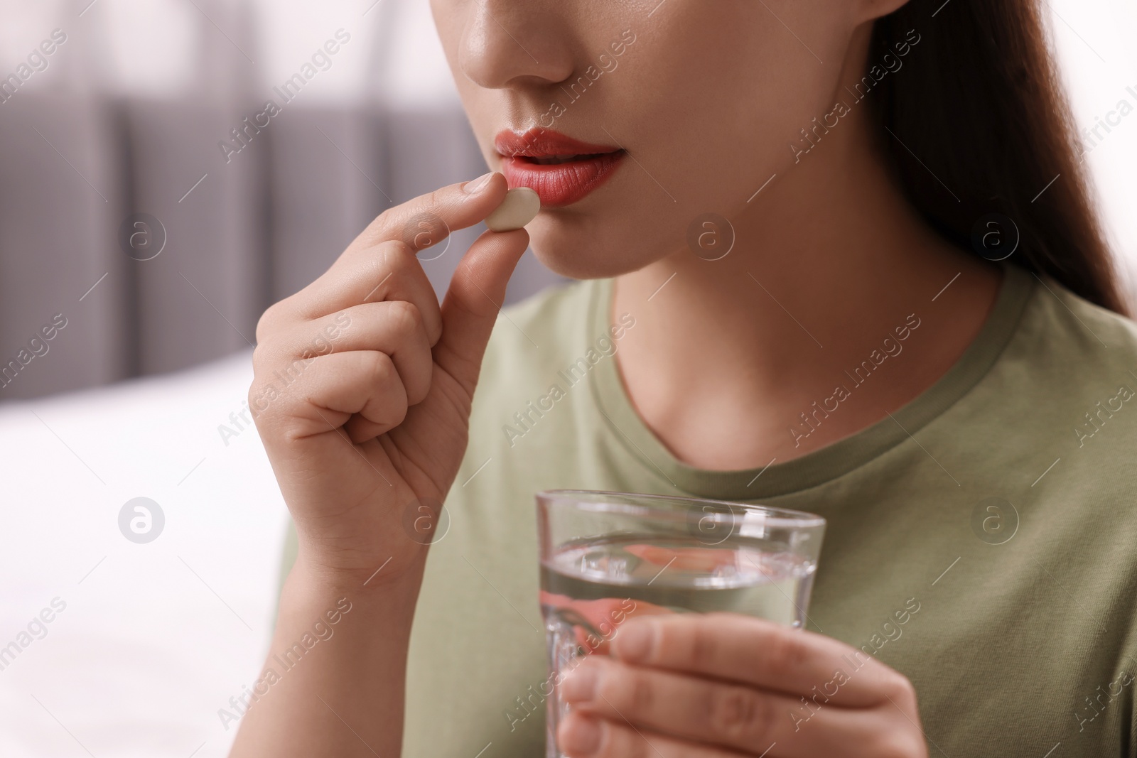 Photo of Woman with glass of water taking antidepressant pill indoors, closeup