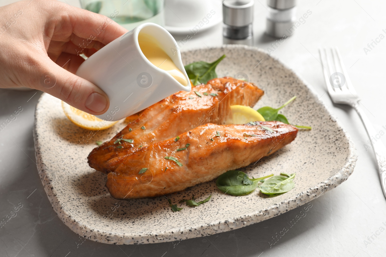 Photo of Woman pouring sauce onto tasty cooked salmon on plate, closeup