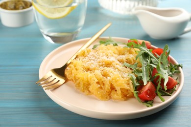 Photo of Tasty spaghetti squash with tomatoes, cheese and arugula served on light blue wooden table