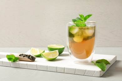 Photo of Glass with aromatic mint tea, fresh leaves and lime on wooden board