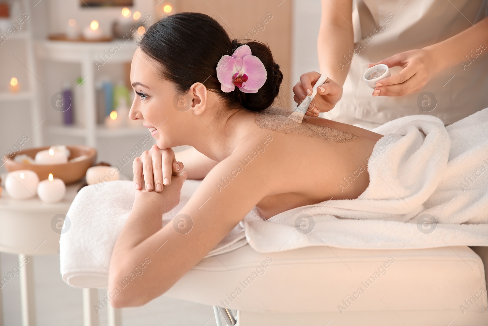 Photo of Beautiful young woman having massage with body scrub in spa salon