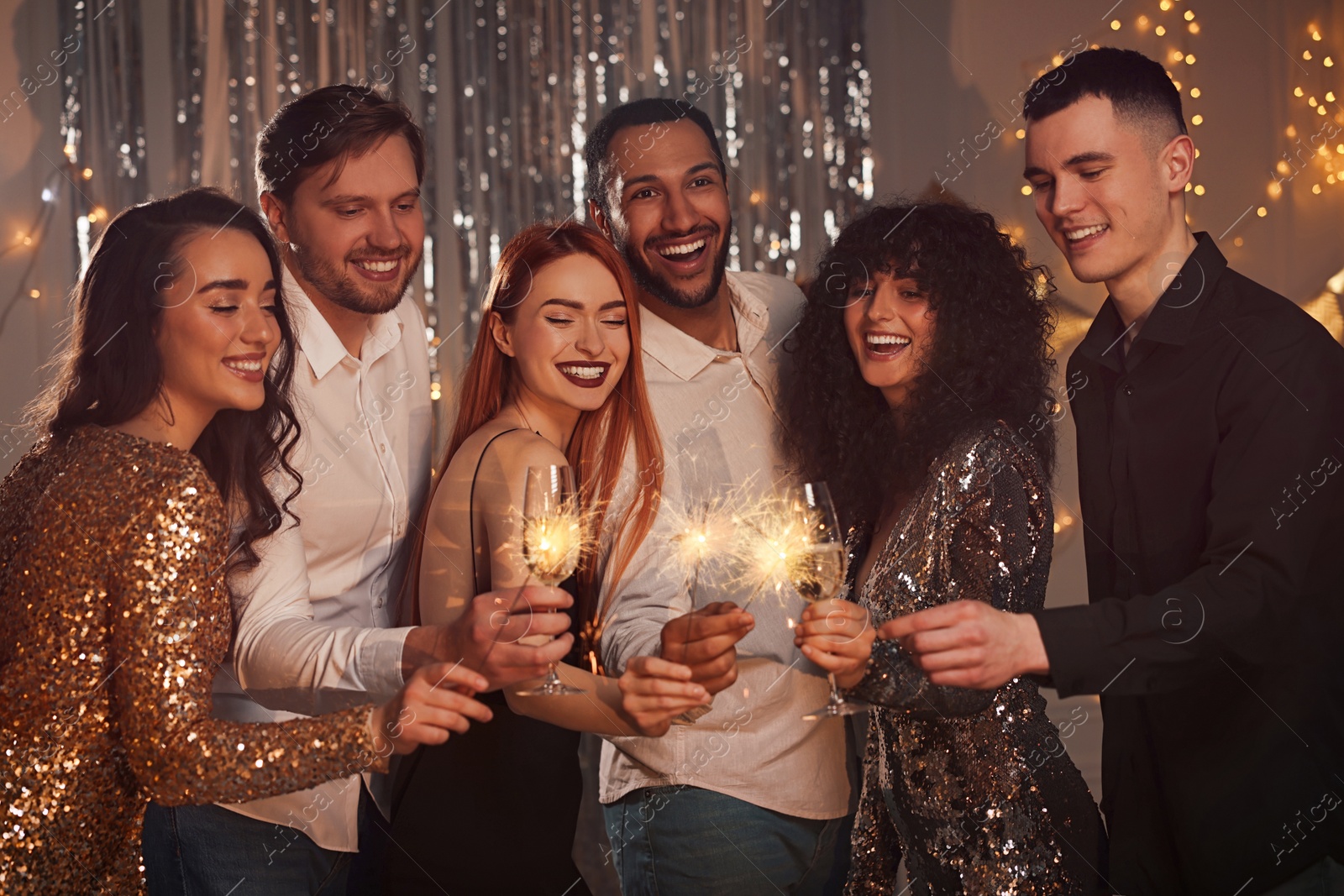 Photo of Happy friends with glasses of wine and sparklers celebrating birthday indoors