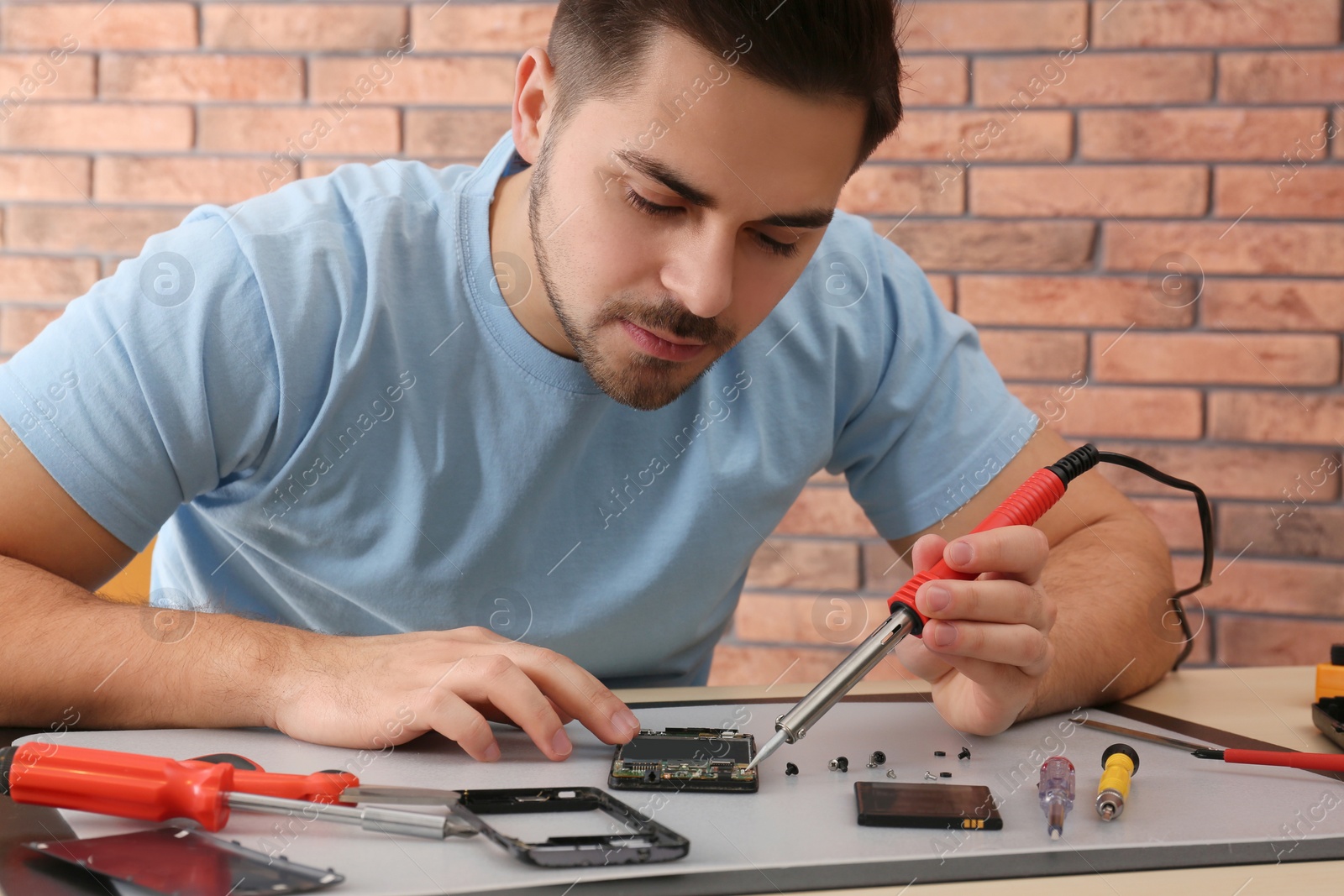 Photo of Technician repairing broken smartphone at table in workshop