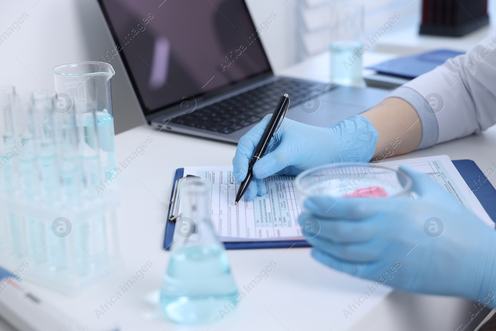 Photo of Laboratory worker holding petri dish with blood sample while working at white table, closeup