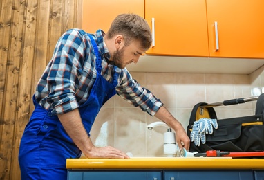 Professional plumber in uniform fixing kitchen sink