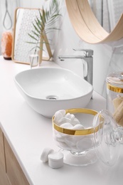 Glass jars with cotton pads and loofahs on table in bathroom