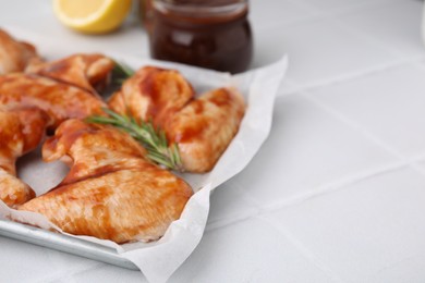 Photo of Raw marinated chicken wings and rosemary on light tiled table, closeup. Space for text