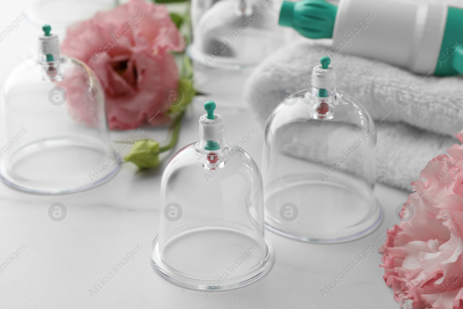 Photo of Plastic cups, flowers and towel on white marble table. Cupping therapy