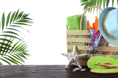 Bag with different beach objects on wooden table against white background. Space for text