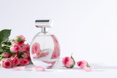 Bottle of luxury perfume and beautiful roses on white background, space for text. Floral fragrance