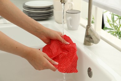 Photo of Woman washing beeswax food wrap under tap water in kitchen sink, closeup