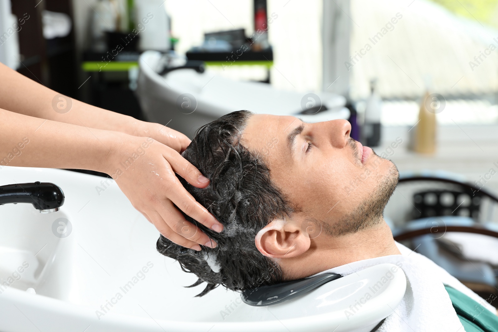 Photo of Stylist washing client's hair at sink in beauty salon