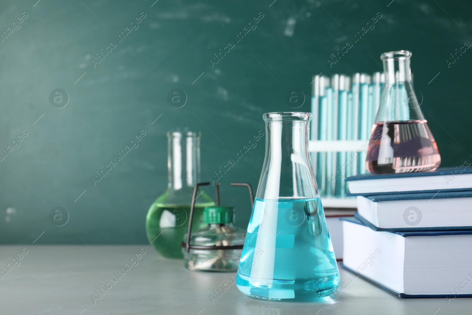 Photo of Laboratory equipment and books on table near chalkboard with space for text. Chemistry concept