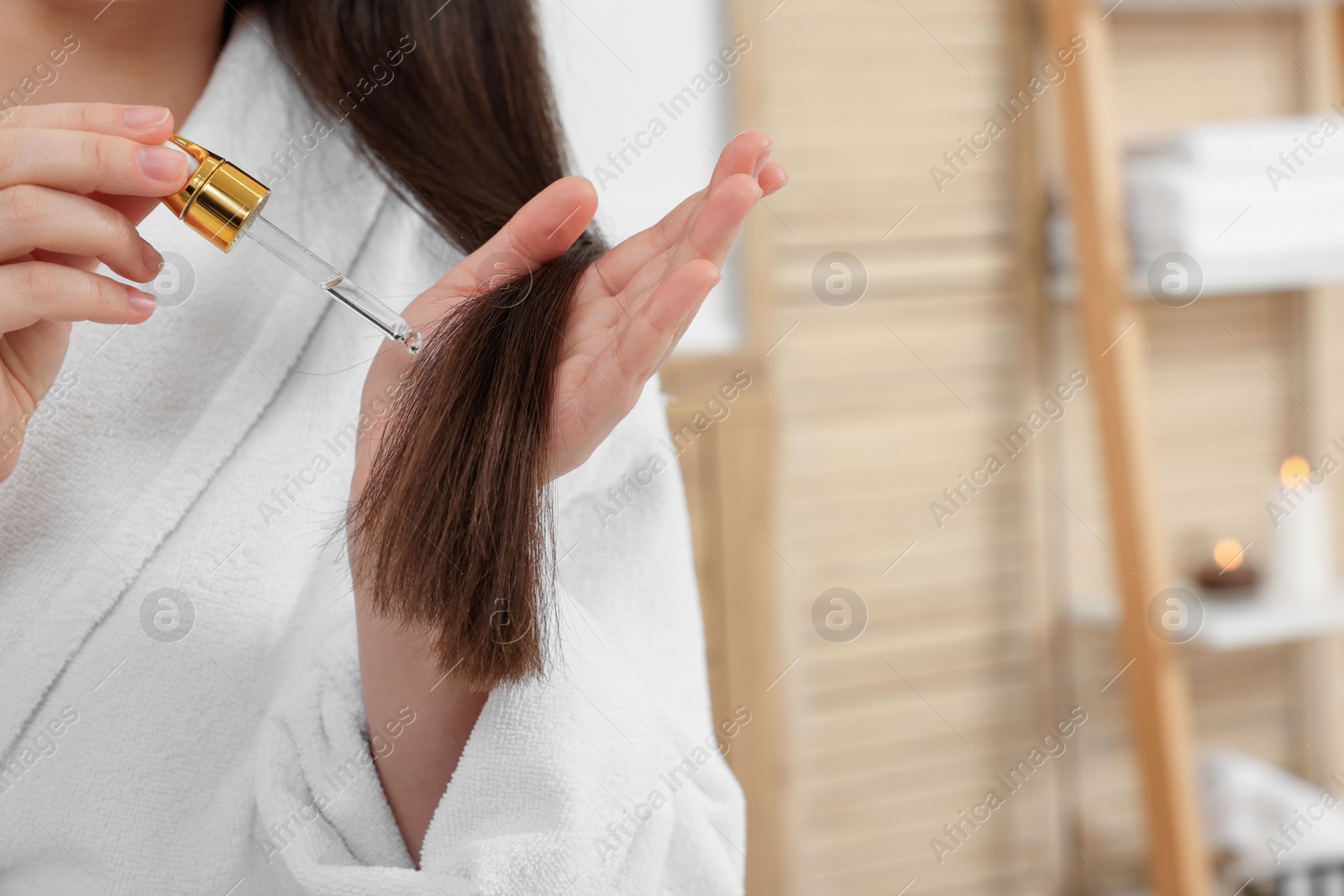 Photo of Woman applying essential oil onto hair in bathroom, closeup and space for text