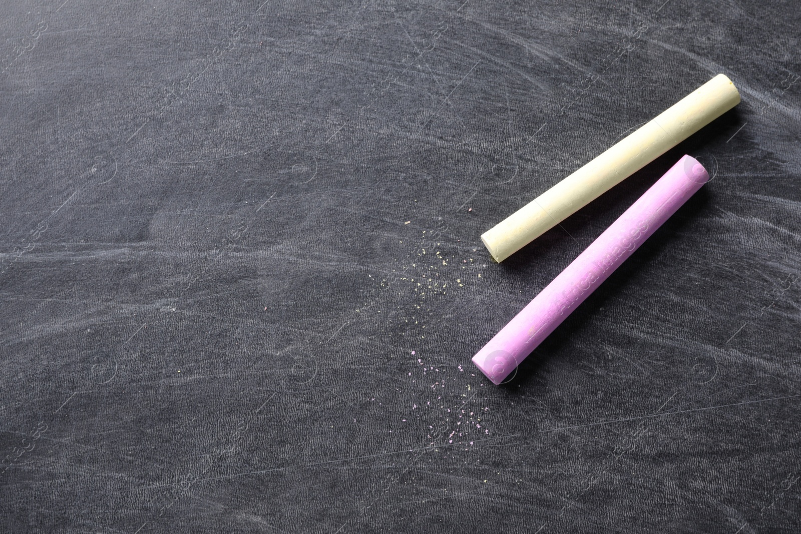Photo of Pieces of color chalk on blackboard, flat lay. Space for text