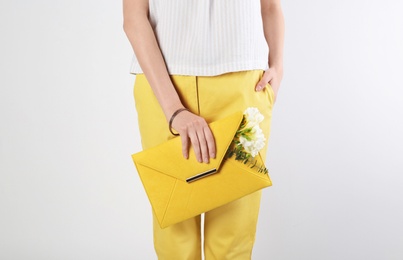 Photo of Stylish woman with clutch and spring flowers against light background, closeup