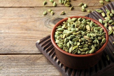 Photo of Bowl of dry cardamom pods on wooden table, space for text