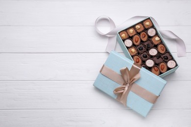 Photo of Open box of delicious chocolate candies and color ribbon on white wooden table. flat lay. Space for text