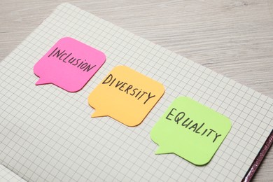 Photo of Sticky notes with words Diversity, Equality, Inclusion and notebook on wooden table, closeup