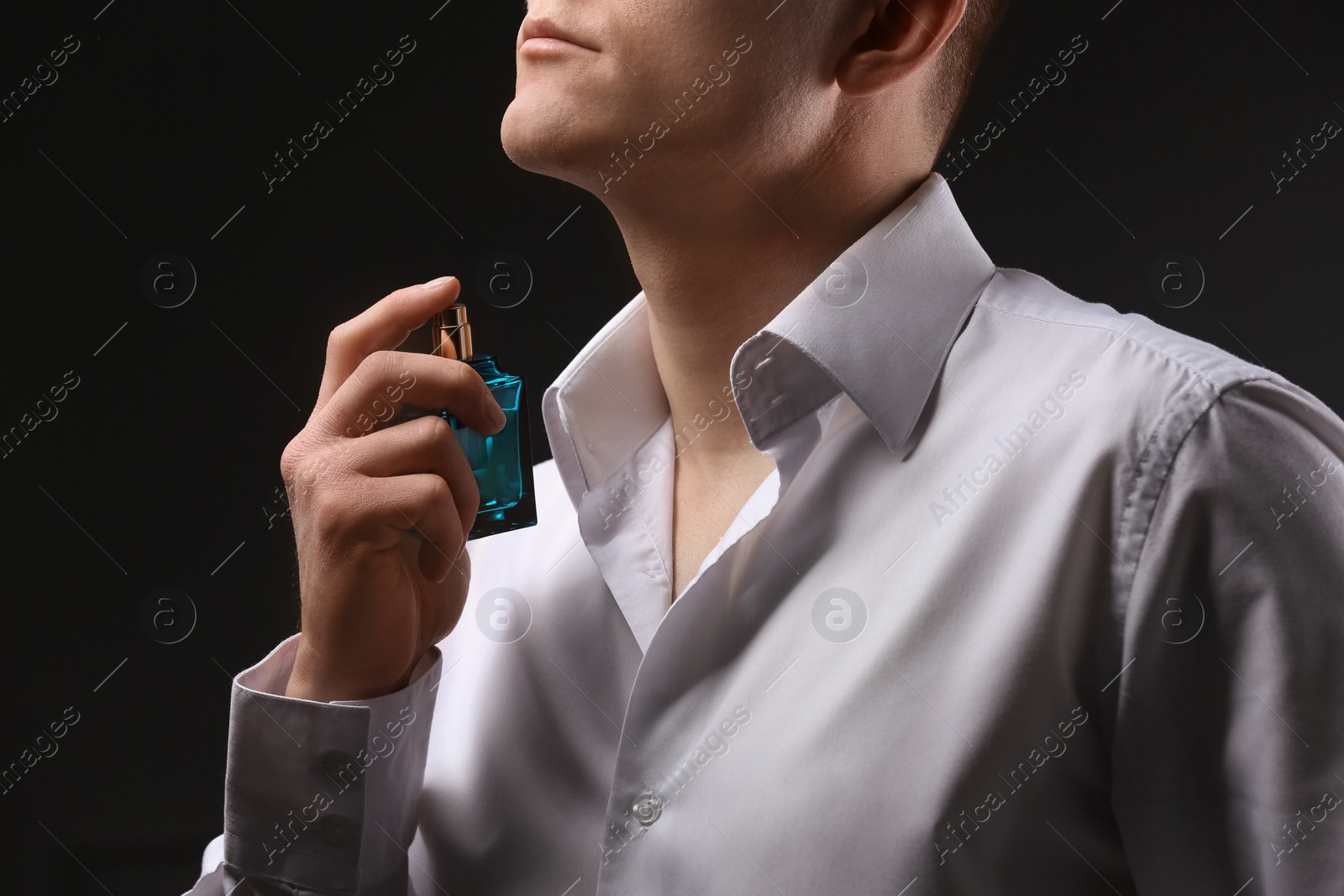 Photo of Handsome man in shirt using perfume on dark background, closeup