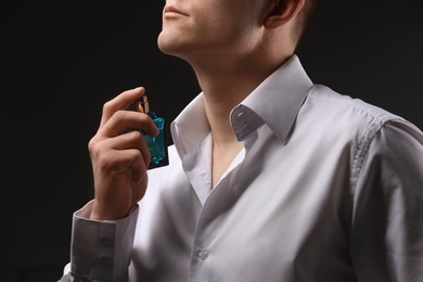 Handsome man in shirt using perfume on dark background, closeup